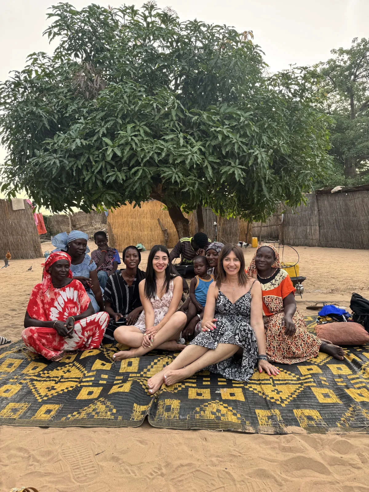 Turiste italiane e donne locali sedute insieme su un tappeto in un villaggio senegalese
